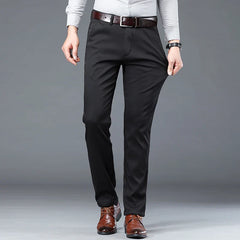 A person wearing a light gray long-sleeve shirt, black dress pants with a tailored fit, a brown belt, and brown dress shoes stands against a plain gray background. Their hands are resting at their sides.