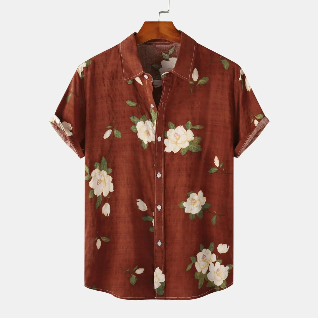 A short-sleeve, button-up linen shirt with a brown background featuring a white floral print and green leaves, displayed on a wooden hanger against a plain white background—perfect for effortless summer style.