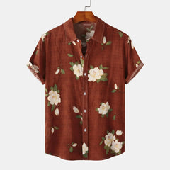 A short-sleeve, button-up linen shirt with a brown background featuring a white floral print and green leaves, displayed on a wooden hanger against a plain white background—perfect for effortless summer style.