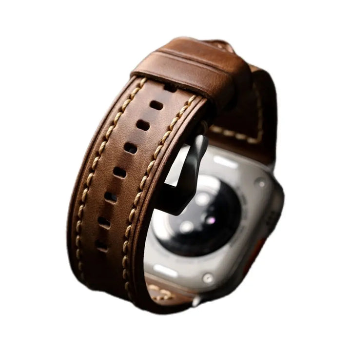 Close-up of a handcrafted brown cowhide leather watch band with cream-colored stitching, attached to a silver smartwatch, displayed on a white background.