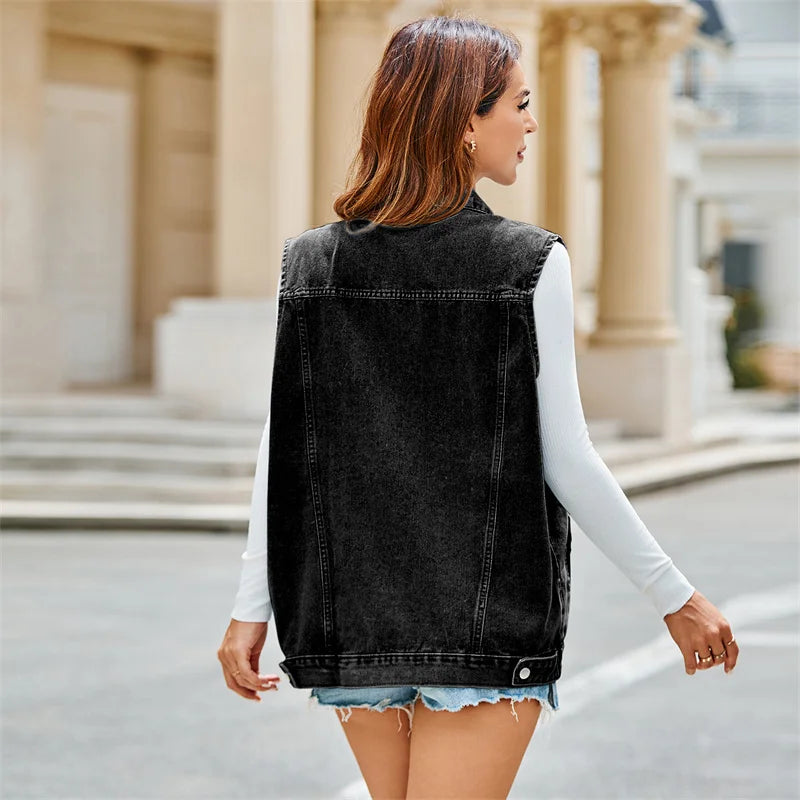 A woman with shoulder-length brown hair, wearing a lightweight breathable sleeveless denim vest over a white long-sleeve top and denim shorts, is walking outdoors near a building with columns.