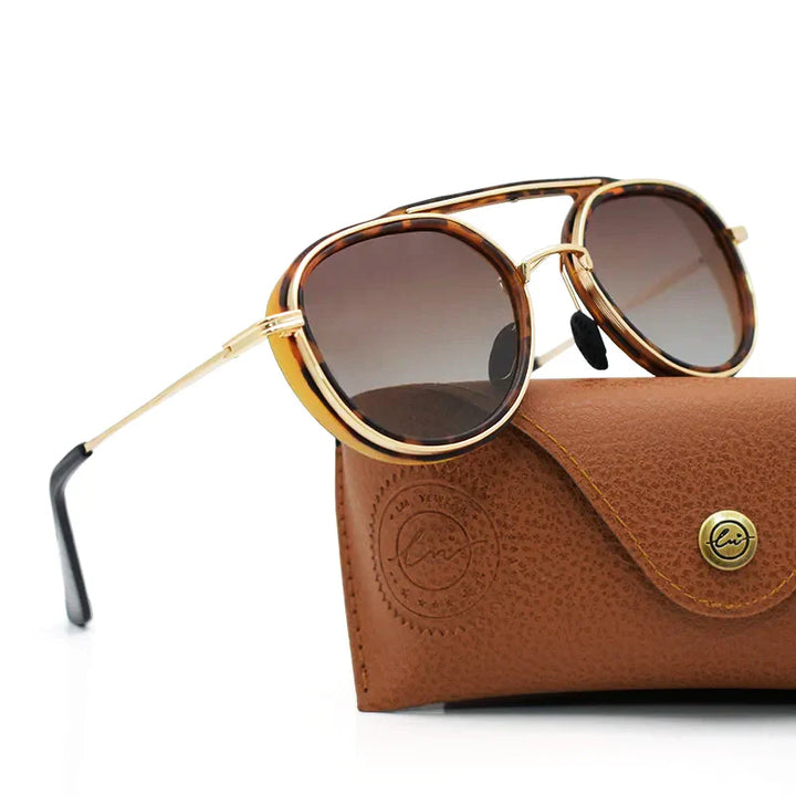 A pair of round, tortoiseshell-rimmed polarized sunglasses with gold arms rests on top of a brown, textured leather case with a button closure on a white background.