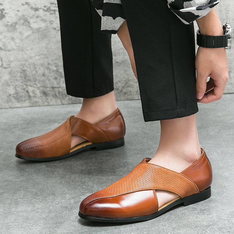 A person wearing stylish brown genuine leather loafers with black dress pants, adjusting one shoe, while standing on a gray stone floor.
