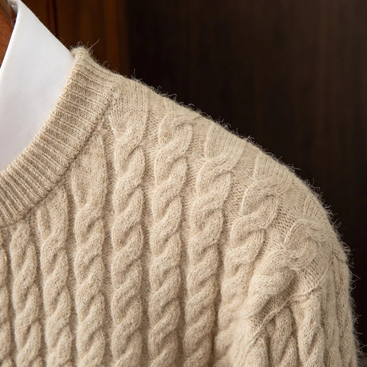Close-up of a beige cashmere cable-knit sweater worn over a white collared shirt, showing the detailed texture, pattern of the knit fabric, and ribbed cuffs.