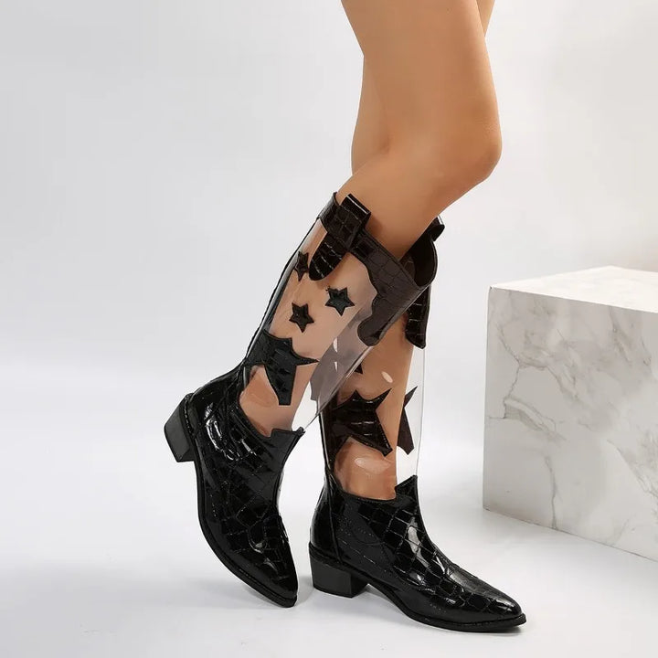 A person wearing knee-high black clear panel boots with black star designs stands against a white background, with a marble-patterned block beside them.