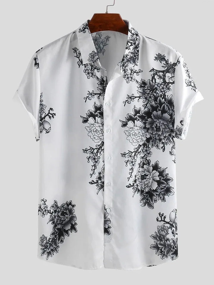 A short-sleeved white floral design shirt with a black pattern of large flowers and leafy branches, crafted from a cotton-silk blend, displayed on a wooden hanger against a plain light gray background.
