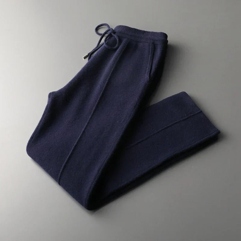 Navy blue knit sweatpants in a tailored pencil cut, featuring an elastic waistband and drawstring, folded neatly on a gray surface.