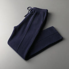 Navy blue knit sweatpants in a tailored pencil cut, featuring an elastic waistband and drawstring, folded neatly on a gray surface.