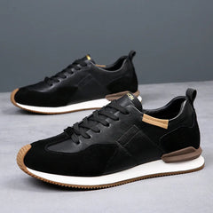 A pair of stylish black sneakers with white midsoles, brown accents on the heel and tongue, and black laces—crafted with top-grain leather—displayed on a gray surface with a plain gray background.
