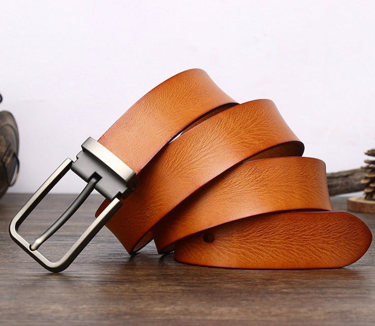 A light brown cowhide belt with a silver metal buckle is coiled on a wooden surface, with the background out of focus.