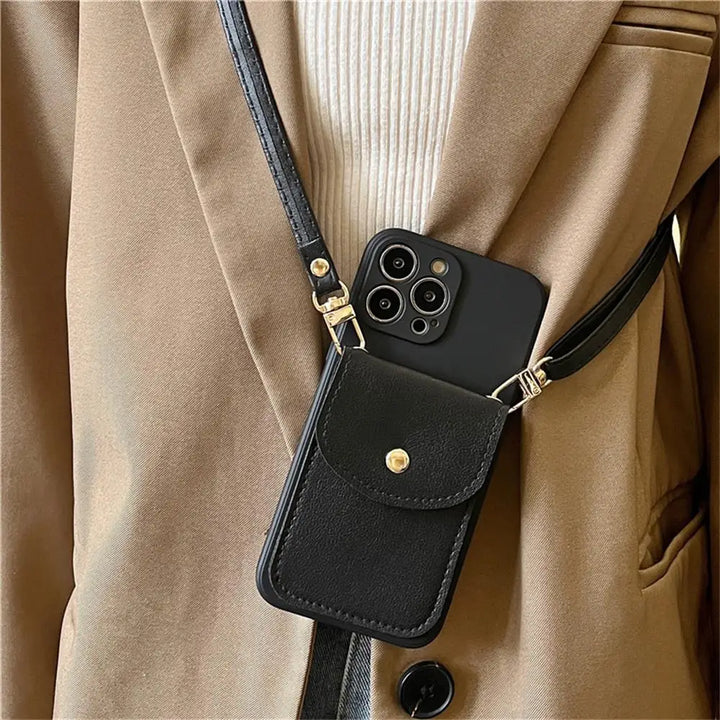 A person wearing a beige coat and white sweater has a black phone case wallet with a pouch and gold button slung across their body on a leather detachable strap. The phone is partially visible, showing its camera lenses.