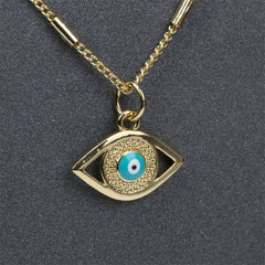 A gold evil eye necklace featuring a textured eye-shaped pendant with a blue and white circular design and shimmering zirconia stone accents, displayed on a dark background.