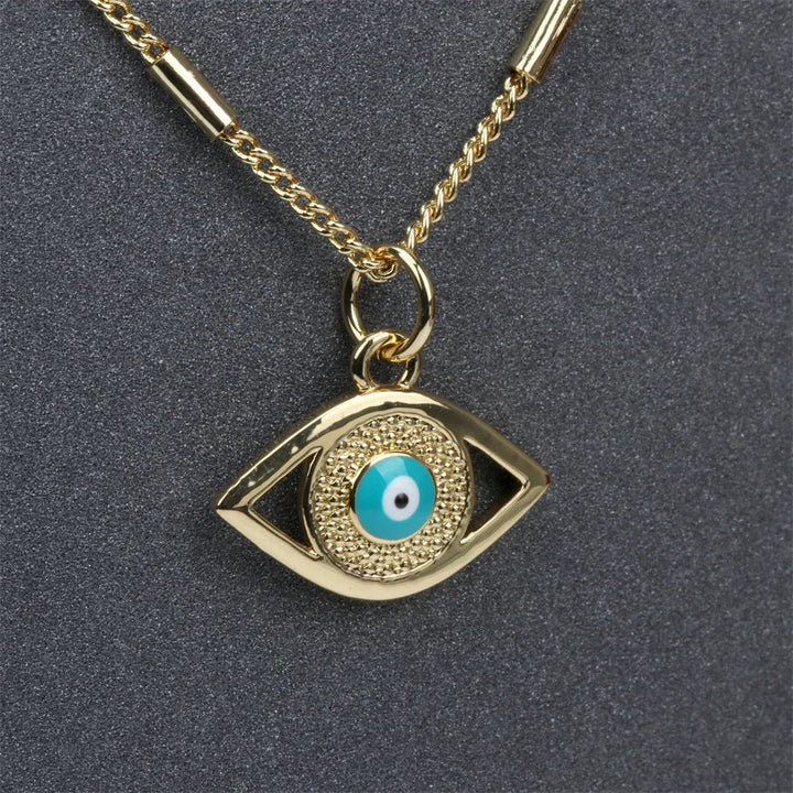 A gold evil eye necklace featuring a textured eye-shaped pendant with a blue and white circular design and shimmering zirconia stone accents, displayed on a dark background.