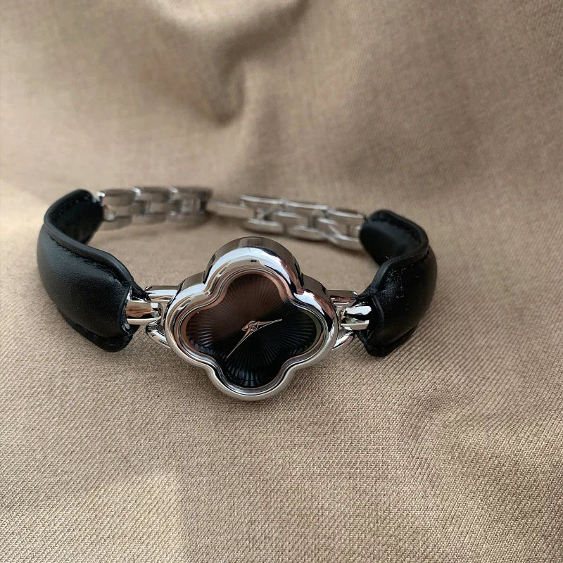 A luxury gold-plated clover dial watch with a black face and genuine leather strap is displayed on a beige fabric background.