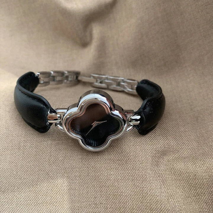 A luxury gold-plated clover dial watch with a black face and genuine leather strap is displayed on a beige fabric background.