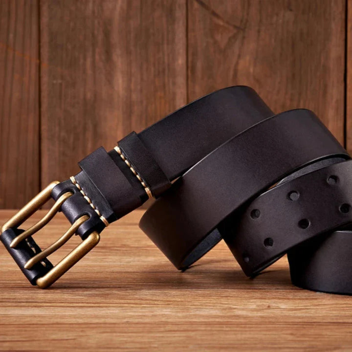 A durable cowhide leather belt with a copper buckle is coiled on a wooden surface, set against a wooden wall in the background.