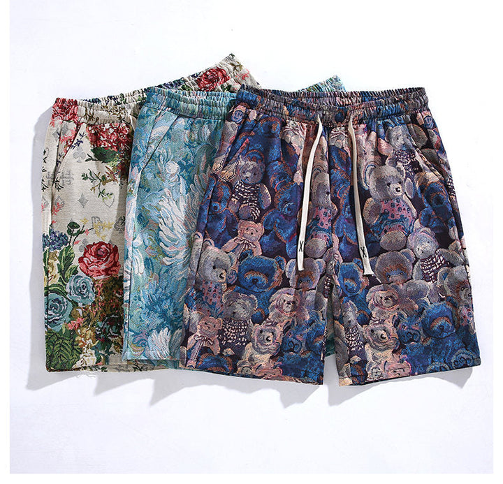 Three pairs of premium quality shorts with different patterns: one with floral designs, one with light blue feathers, and one with teddy bears on a dark blue background, displayed overlapping on a white surface.