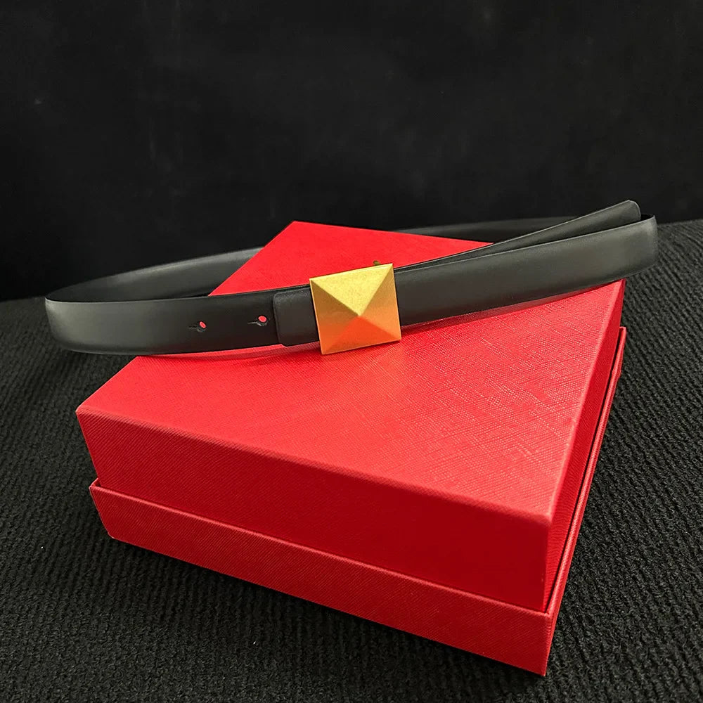 A leather belt with a large gold buckle and adjustable length rests on a closed, textured red box against a black background.