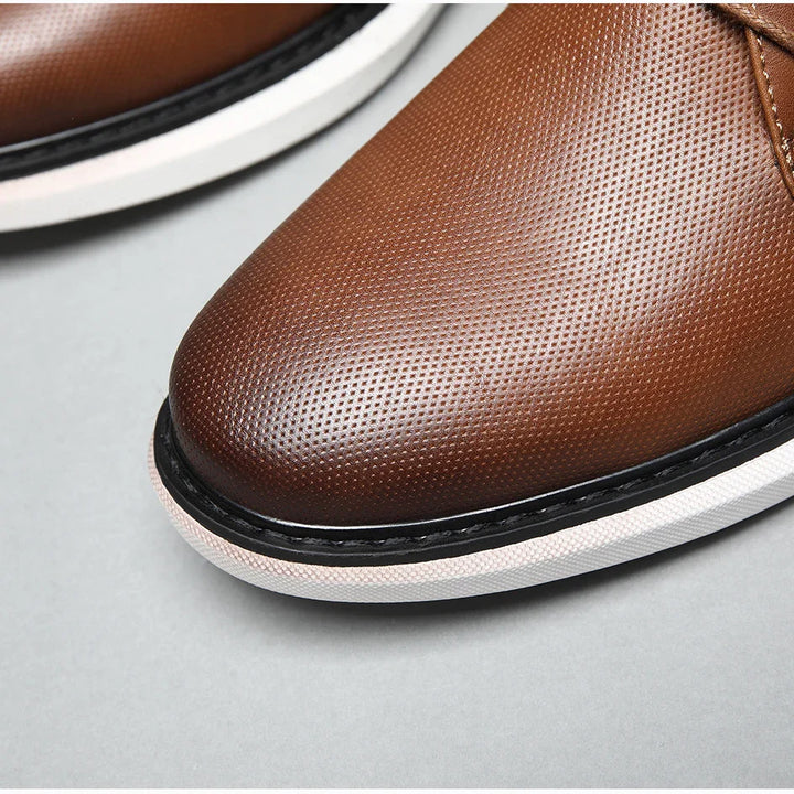 Close-up of the front part of a luxury mens shoe in brown perforated leather with traditional detailing, featuring white and black soles against a light gray background.