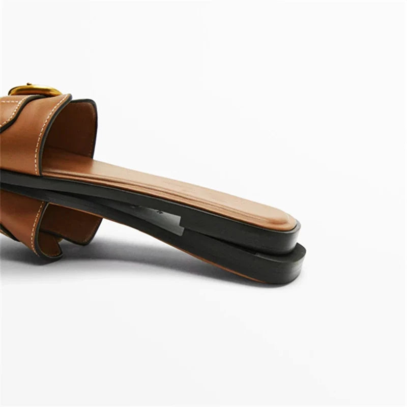 Close-up of a brown leather slide sandal with a flat, rectangular sole and a slight platform, displayed on its side against a plain white background.