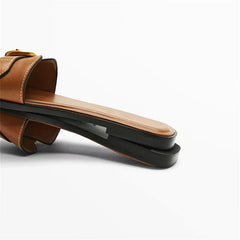 Close-up of a brown leather slide sandal with a flat, rectangular sole and a slight platform, displayed on its side against a plain white background.