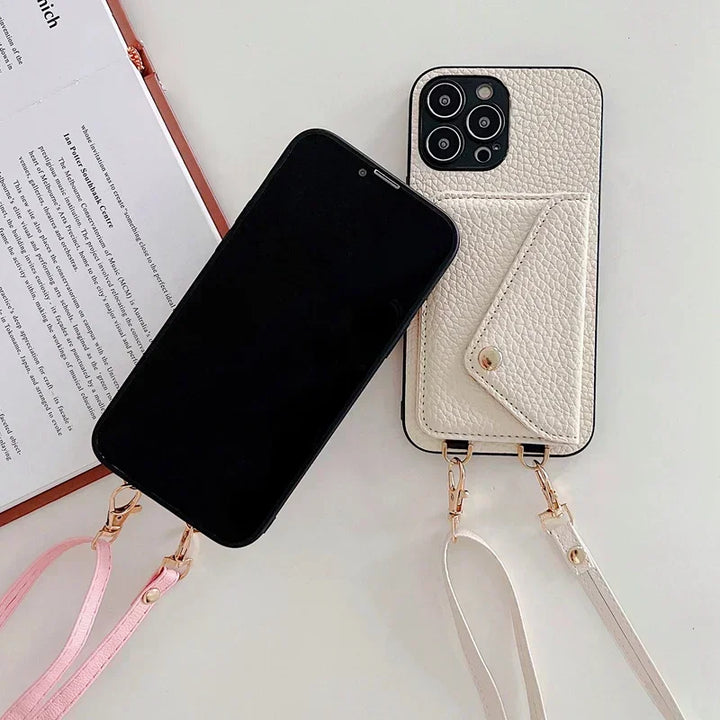 Two smartphones with attached strap holders are shown; one features a pink strap and black screen, while the other has a white pebble-texture material case with a cardholder pocket, a white strap, and its camera lenses visible. An open book lies nearby.