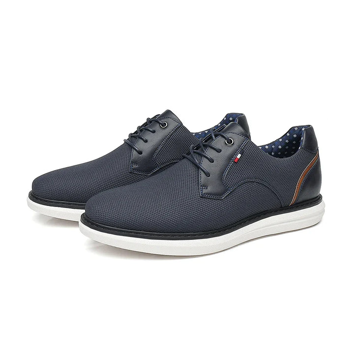 A pair of dark blue lace-up casual shoes with white soles, textured uppers, and a small brown accent on the heel. The inner lining is blue with white polka dots, blending traditional detailing with modern style.