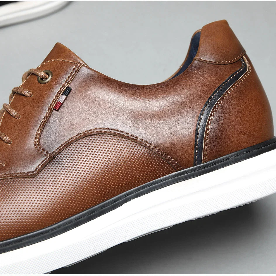 A close-up of a brown genuine leather oxford casual shoe with perforated traditional detailing, white sole, black trim, and decorative stitching, shown against a gray background.