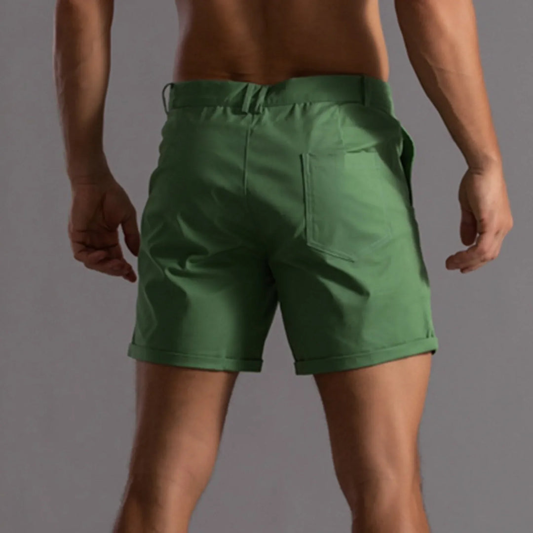 A person shown from the back wearing green shorts with a tailored fit, standing against a plain, neutral-colored background. The shorts have a cuffed hem, visible back pocket, and a semi elastic waistband for added comfort.