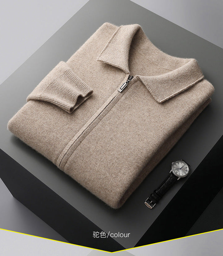A beige merino wool zip-up sweater with a folded collar and cuff is neatly folded on a dark gray surface. A black leather-strap wristwatch lies next to it. The word colour appears at the bottom.