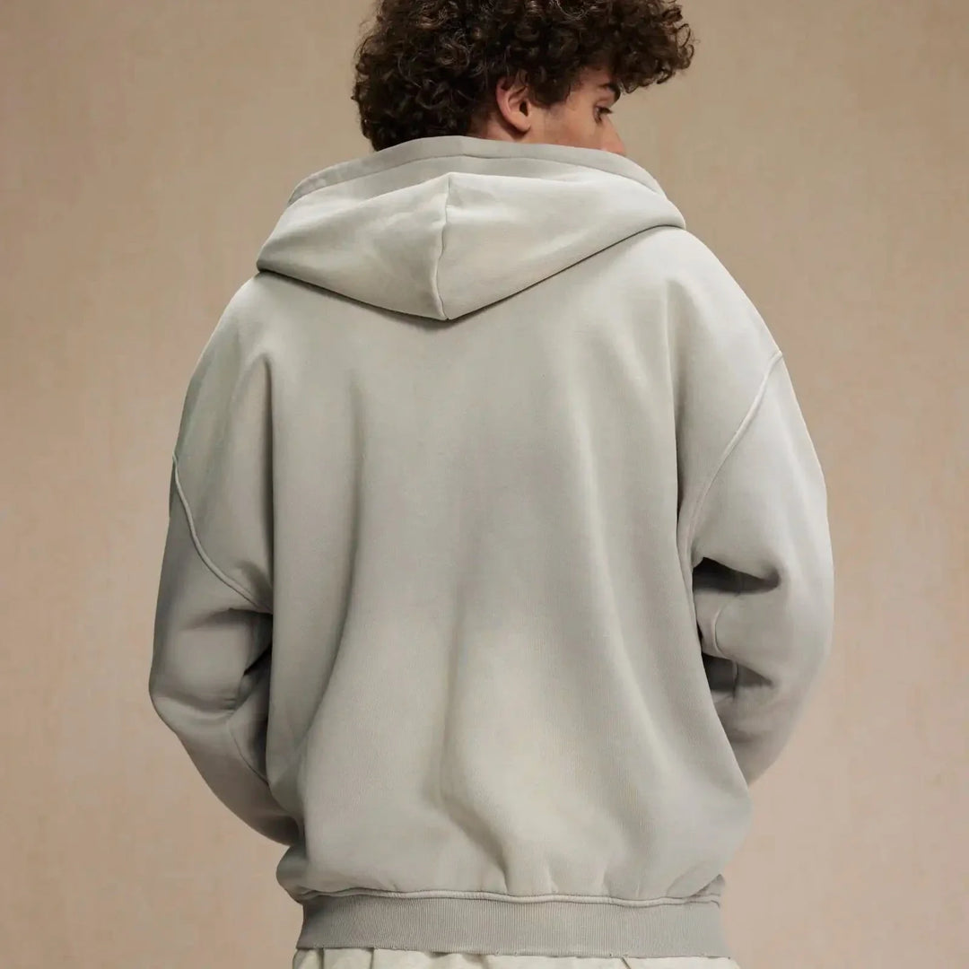 A person with curly hair is wearing a relaxed fit, light gray hoodie made from thickened fabric, standing with their back to the camera against a plain beige background.