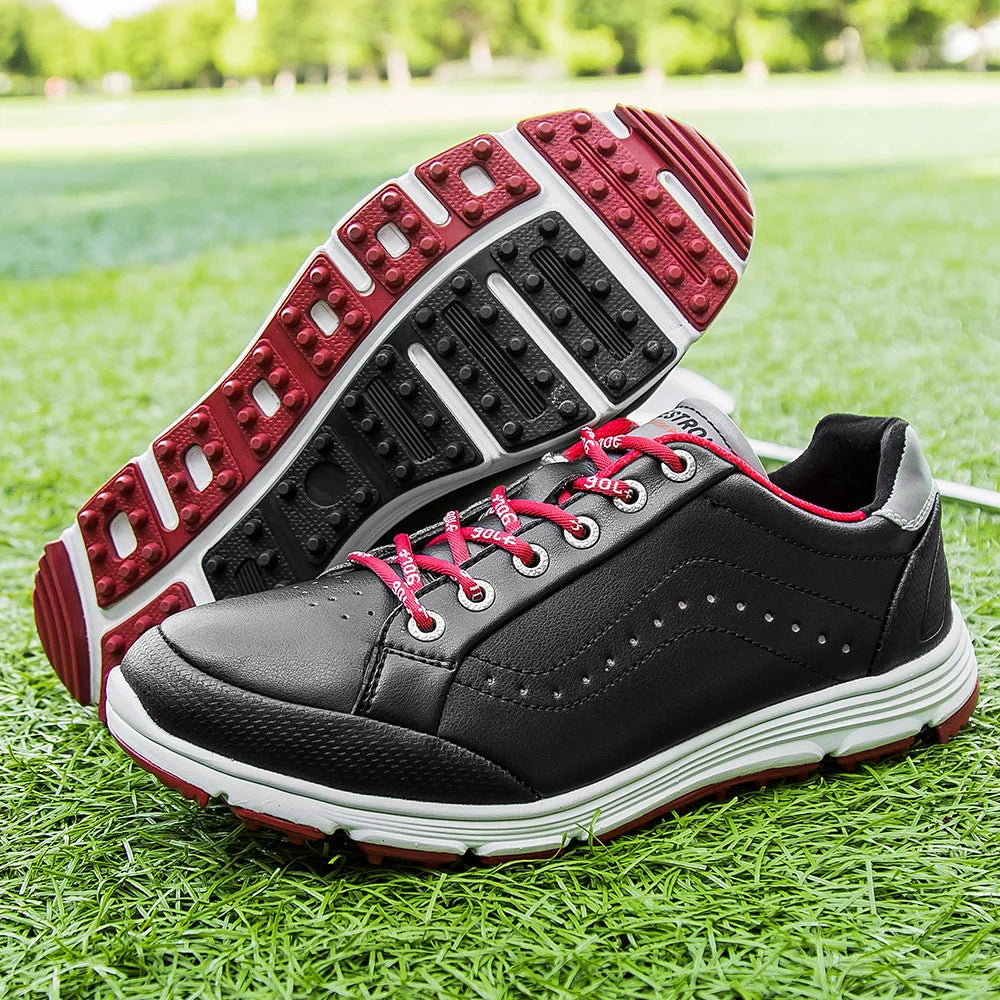 A pair of black waterproof golf shoes with red laces and red-and-white soles, featuring advanced cleat technology, displayed on green grass—one shoe upright and the other showing its tread pattern.