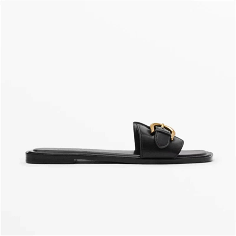 A black leather slide sandal with an open toe and a gold buckle detail on the strap, shown in a side profile view against a plain white background for an easy slip-on style.