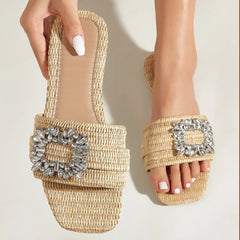 A person wearing handwoven cane slip-on flats with square toes and decorative silver buckles, showing a close-up of their feet with white-painted nails on a light background.