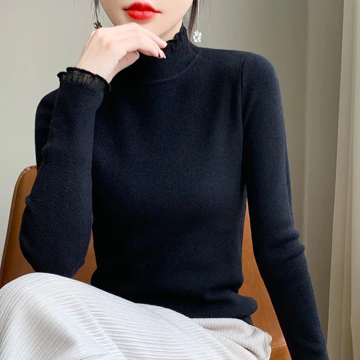 Woman sitting on a chair, wearing a fitted black cashmere blend turtleneck sweater and light-colored pants. Her hand is near her chin, with red lipstick and dangling earrings. Her face is partially visible.