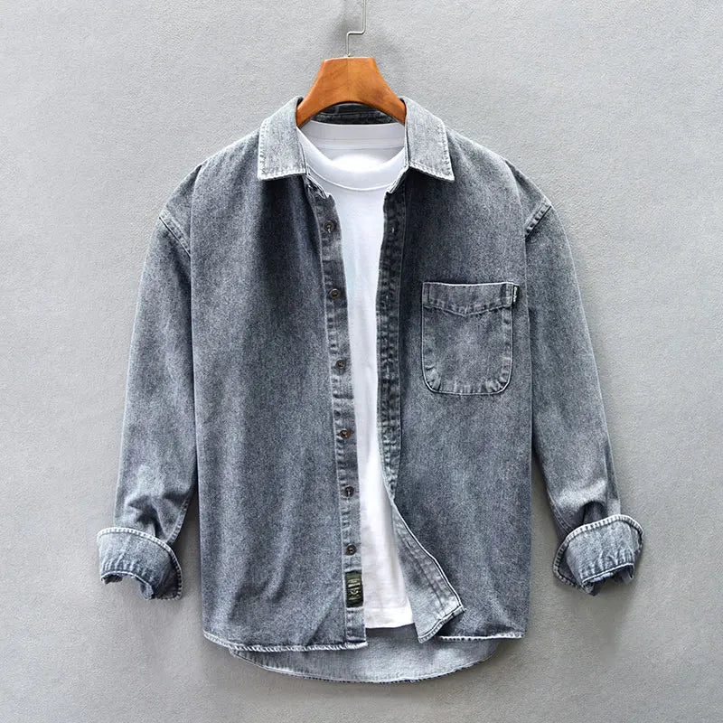 A washed denim button-up overshirt with rolled-up sleeves is layered over a plain white T-shirt and displayed on a wooden hanger against a light gray background.