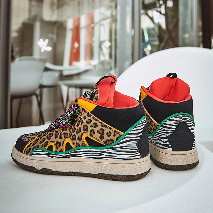 A pair of colorful animal print shoes with leopard print, zebra stripes, bright orange lining, green accents, and multicolored laces, featuring durable rubber soles, displayed on a white surface indoors with chairs and windows in the background.