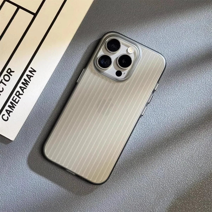 A smartphone with a silver, vertically striped titanium phone case lies on a gray surface next to part of a paper that reads DIRECTOR and CAMERAMAN. The slim lightweight design features three rear cameras.