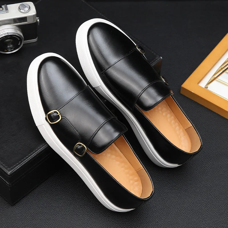 A pair of black leather Slip-On Loafers with white soles and gold buckle details, displayed on a black textured surface next to a vintage camera and a yellow-edged stack of books, captures timeless British Fashion.