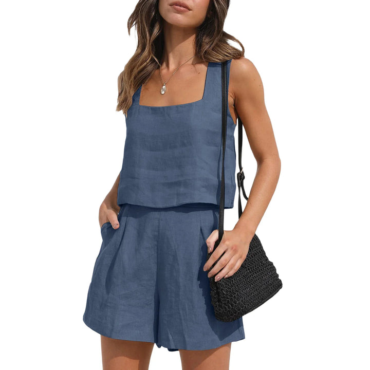 A woman wears a contemporary style blue linen set featuring a sleeveless vest with a square neckline and matching shorts, holding a black woven crossbody bag. The background is white.