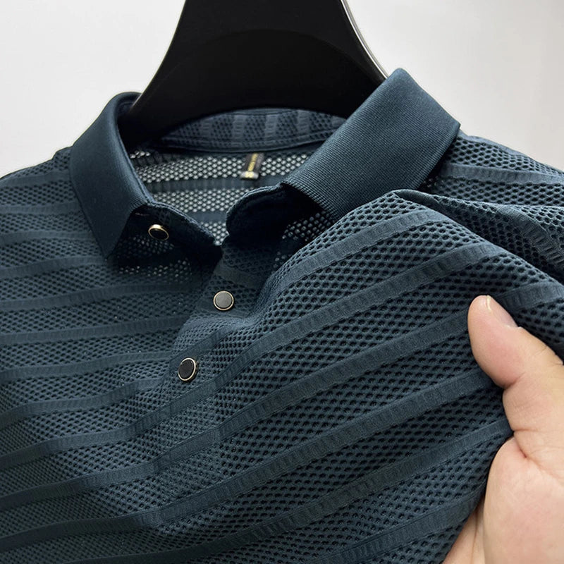 A close-up of a dark blue, short-sleeve, classic polo shirt with textured, striped, and breathable mesh fabric, held up by a hand on a hanger.