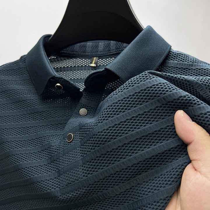 A close-up of a dark blue, short-sleeve, classic polo shirt with textured, striped, and breathable mesh fabric, held up by a hand on a hanger.