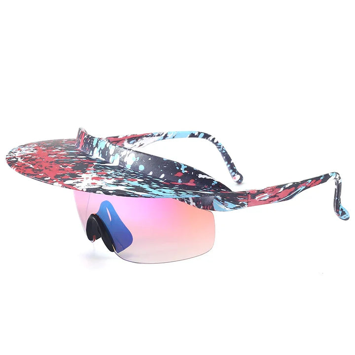 A visor-style pair of sunglasses with a wide, colorful, paint-splattered brim in red, blue, and black. The attached lens is tinted pink and fades to clear, featuring adaptive design and blue nose pads.