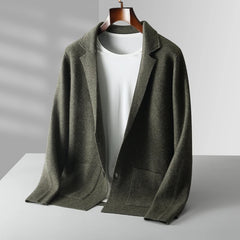A casual men’s wool cardigan in olive green with front pockets is draped over a hanger, layered over a plain white T-shirt—a perfect autumn winter knit on a minimal gray background.