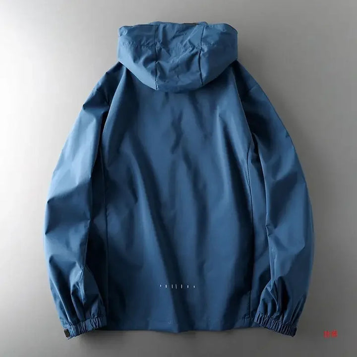 A blue breathable outdoor jacket laid flat on a gray surface, shown from the back with long sleeves and elastic cuffs.