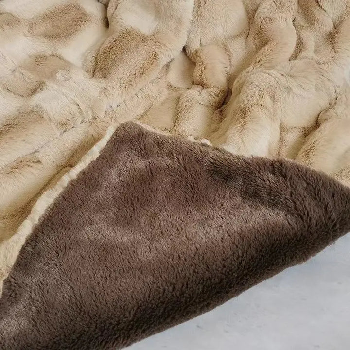 A soft, plush faux mink blanket with a light beige, textured pattern on one side and smooth, solid brown fabric on the other, lying on a flat surface.