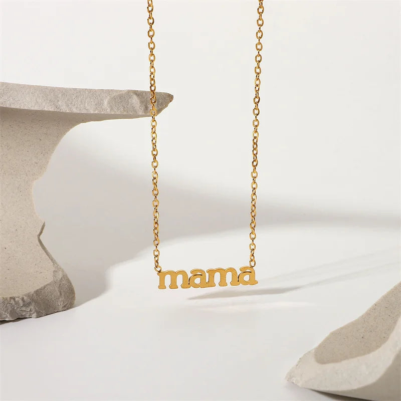 A gold mama pendant necklace with the word mama in lowercase letters hangs between two abstract pieces of light-colored stone on a white background. Perfect as a Mothers Day necklace for celebrating moms every day.