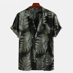 A classic design, short-sleeve cotton shirt with a black background and a green fern leaf pattern. Perfect for a casual brunch, its displayed on a wooden hanger against a plain white background.