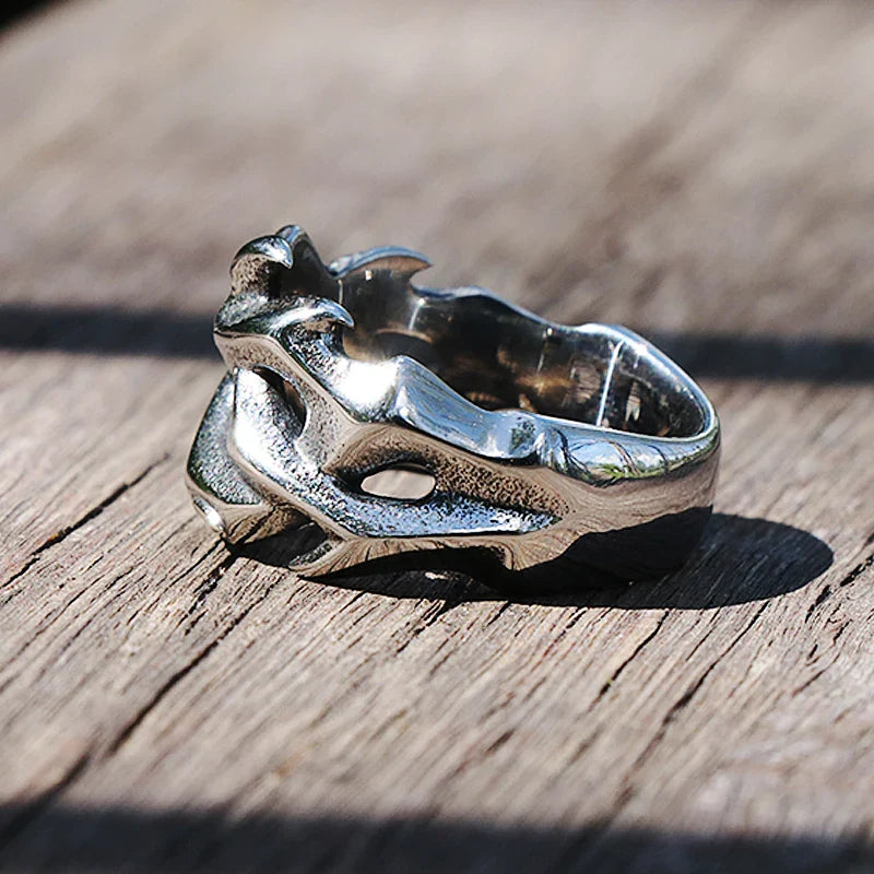 A silver streetwear ring designed to resemble a dragon’s head, featuring detailed scales and horns, rests on a wooden surface—a bold statement piece in fashion jewelry.