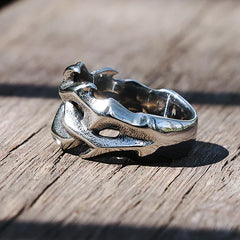 A silver streetwear ring designed to resemble a dragon’s head, featuring detailed scales and horns, rests on a wooden surface—a bold statement piece in fashion jewelry.